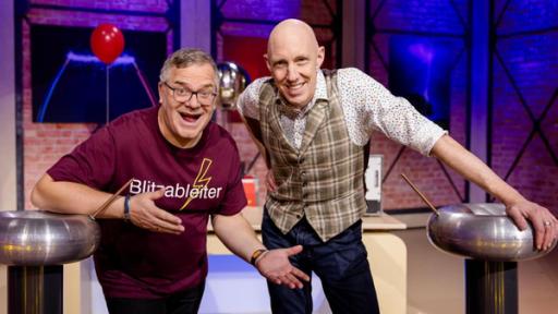 Elton (l.) und Markus Weber (r.) stehen zwischen zwei Exponaten im Studio und grinsen in die Kamera.