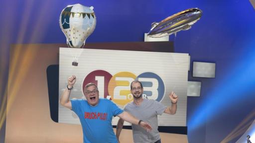 Elton und Benjamin Bachmaier stehen im Studio auf einem Bein und halten jeweils einen mit Gas gefüllten Luftballon über ihre Köpfe.