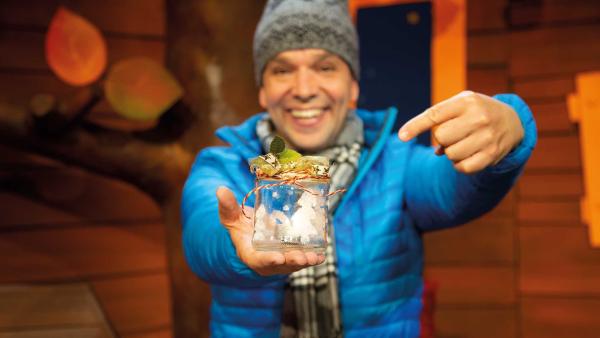 Juri vom "KiKA Baumhaus" hält ein selbstgemachtes Schneeglas in der Hand. Auf dem Glas ist en Tannenbaum aus Salz zu sehen. Es mit einer Schnur und kleinen Zweigen geschmückt. | Rechte: KiKA