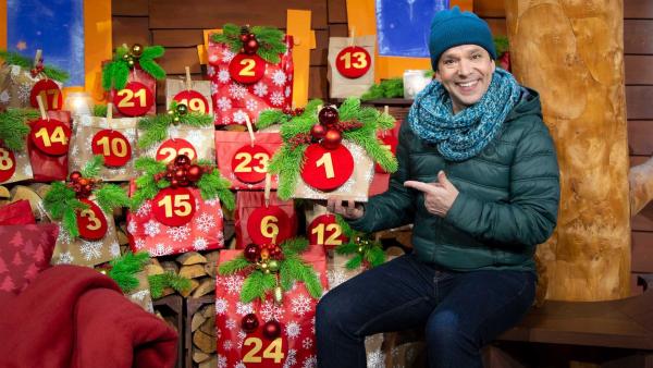 Juri hält ein Päckchen mit der Nummer Eins in der Hand. Hinter ihm ist ein Adventskalender.