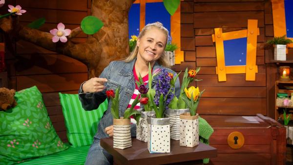 Singa zeigt auf bunte Frühlingsblumen, die vor ihr auf dem Tisch stehen.