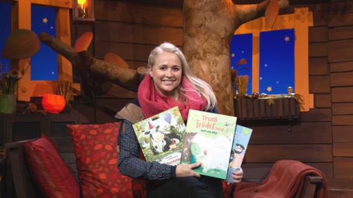 Singa sitzt auf dem Sofa im Baumhaus und hält drei Kinderbücher in der Hand.