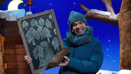 Juri hält eine Tafel in der Hand, auf der Bäume und ein Pfad gemalt sind.