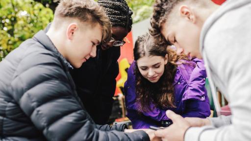 Diana, Anton, Ros und Dasha stehen im Kreis und schauen auf ein Handy