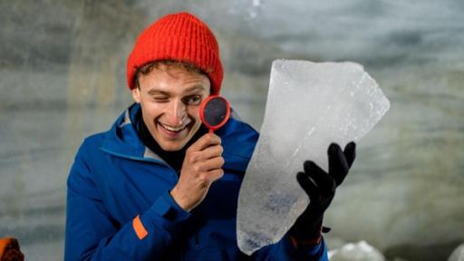 Erforsche den Gletscher | Julian erforscht mit einer Lupe ein Stück Gletschereis. 