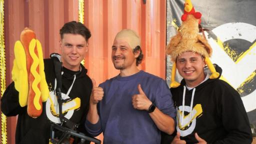 Checkpoint: Das Checkpoint-Team, bestehend aus Jeppe, Moderator Tommy Scheel und Cem, stehen vor dem Checkpoint-Container und präsentieren drei verrückte Badekappen. 