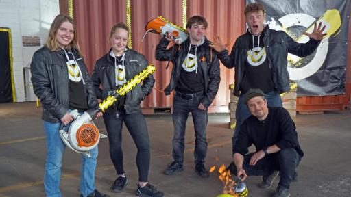 In der Checkpoint-Halle stehen die Testteamer Lisa, Antonia, Felix und Kenneth mit selbstgebauten Laubbläsern in der Hand. Tommy Scheel sitzt vor ihnen in der Hocke; vor ihm ein angezündeter Volleyball. 