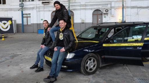 Leopold, Moderator Tommy Scheel und Cem sitzen auf der Motorhaube eines blauen Autos, das in einer alten Industriehalle steht.