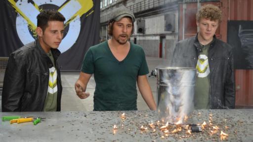 Cem (links), Tommy (mitte) und Kenneth (rechts) stehen vor einem Eimer mit brennenden Steichhölzer in der Checkpoint-Halle.