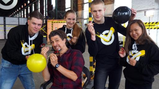 Checkpoint: Tommy Scheel und das Checkpoint Team halten Ballons und Dartpfeile in den Händen.