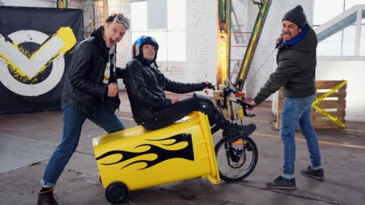 Checkpoint: Tommy Scheel zieht das Checkpoint Team auf einer gelben Mülltonne mit Rädern.