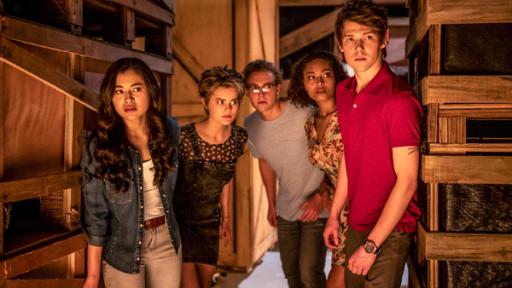 Der Kunstraub | Rechte: c) 2020 Jonathan M. Shiff Productions Kyra (Kimie Tsukakoshi), Imogen (Elizabeth Cullen), Peter (Jamie Carter), Ruksy (Rainbow Wedell) und Darra (Julian Cullen) stehen dicht nebeneinander in einem dunklen Raum zwischen Holzregalen. Sie schauen vorsichtig und aufmerksam in eine Richtung.