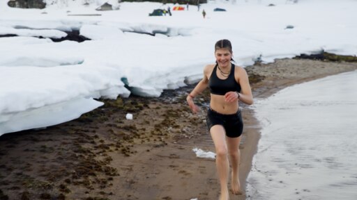 Emilia läuft im Bikini am Strand. Rechts befindet sich das Wasser, links der hohe Schnee. 