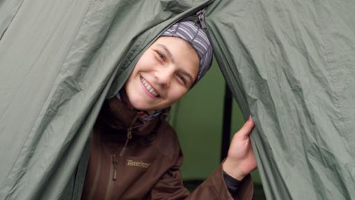 Emilia lächelt in die Kamera. Durch die Öffnung des grünen Zeltes sind ihr Gesicht und Oberkörper zu sehen.