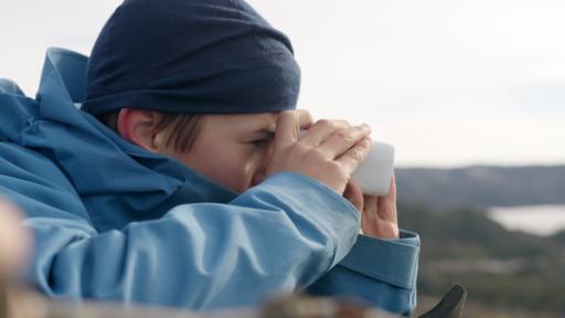 Niklas ist von der Seite zu sehen. Er blickt durch ein Fernglas in die Ferne.