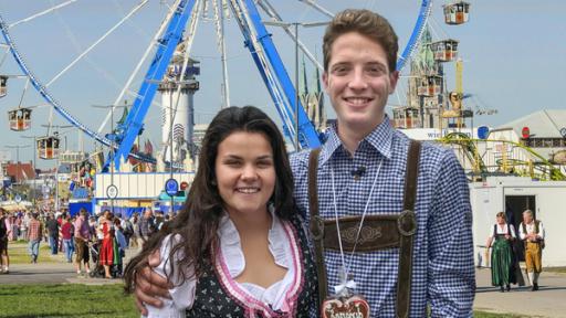 Louisa und Philip posieren in bayerischer Lederkluft vor einem Riesenrad.