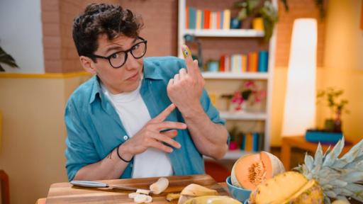 "Das Wunder DU - Wie werde ich gesund?": Christoph sitzt am Tisch und hebt den linken Zeigefinger. Darum ist ein Pflaster gewickelt. Vor ihm auf dem Tisch liegt eine Schneidebrett mit Banane. Davor stehen Schüsseln mit Obst.