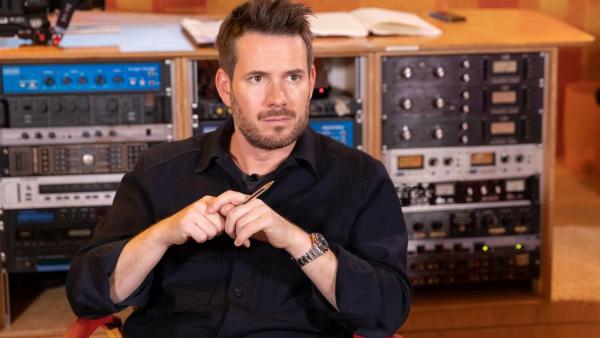 Johannes Strate, sitzt vor vielen technischen Geräten im Tonstudio, hält einen Kugelschreiber in beiden Händen vor dem Körper und denkt nach. | Rechte: ZDF