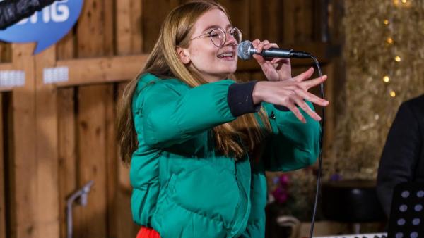 "Dein Song" Kandidatin Fine steht mit dem Mikrofon in der Hand, singend in der "Dein Song" Scheune und streckt ihre rechte Hand nach vorne. | Rechte: ZDF
