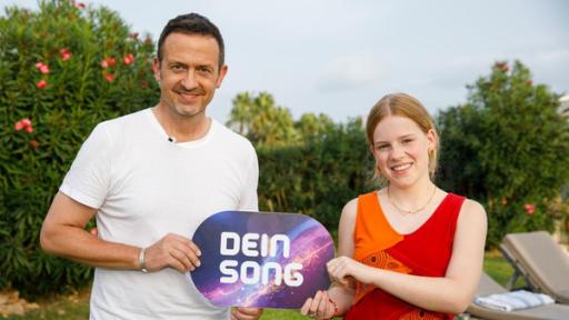 Till Brönner und Frida stehen nebeneinander und halten ein Dein Song-Schild zwischen sich. Sie lächeln.