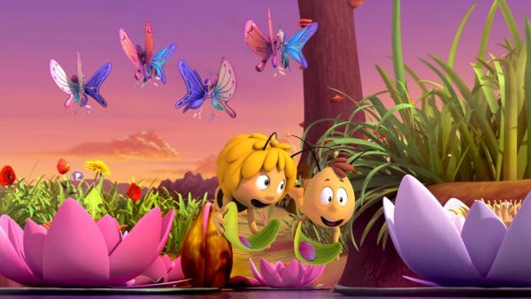 Willi und Maja fliegen glücklich nebeneinander und tragen bunte Blüten auf Blättern. Begleitet werden sie dabei von vielen bunten Schmetterlingen. | Rechte: Nach Waldemar Bonsels “Die Biene Maja”. © 2012 Studio 100 Animation 