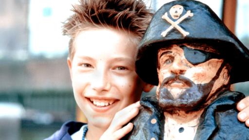 Paul steht neben einer Piratenfigur mit Hut und Augenklappe und legt die Hände auf ihre Schultern.