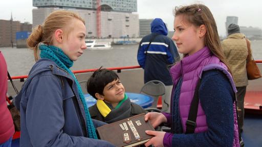 Nina (Carolin Garnier, rechts) übergibt Jessi (Martha Fries, links) und Luis (Emilio Sanmarino, Mitte) das Pfefferkörnerbuch.