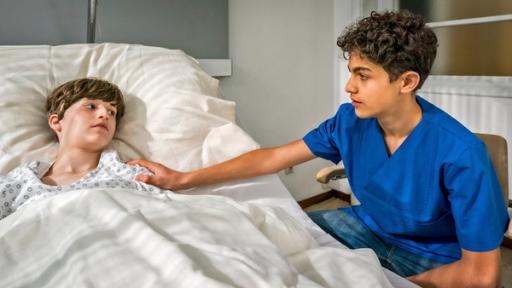 Tarun legt einem Jungen, der in einem Krankenhausbett liegt, eine Hand auf die Schulter.