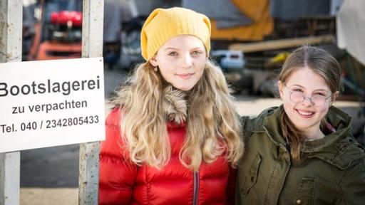 Stella (Zoë Malia Moon) und Pinja (Sina Michel) stehen neben einem Schild der Bootslagerei.