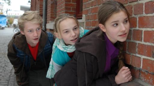 Max (Bruno Alexander), Jessi (Martha Fries) und Nina (Carolin Garnier) halten sich gedeckt an einer Hauswand.