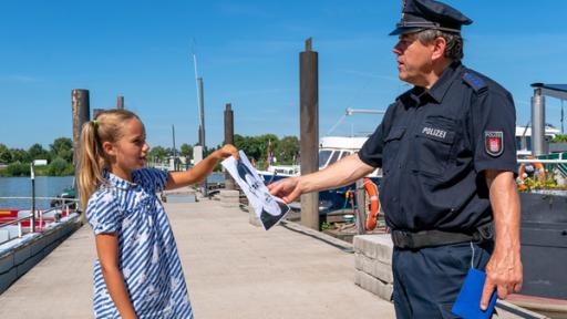 Clarissa überreicht dem Polizisten ein Bild, auf dem das Gesicht eines Mannes zu erkennen ist.