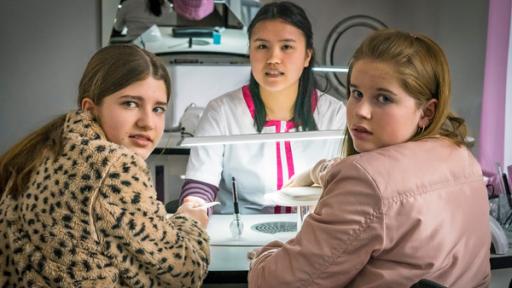 Lou und Pippa sitzen an einem Tisch im Nagelstudio, auf der anderen Seite des Tisches sitzt Mai.