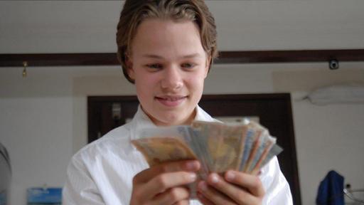 Leon (Luka Krause) hält lächelnd Geldscheine in der Hand.