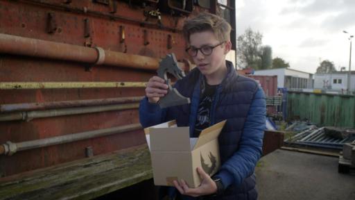 Benny hält ein Karton und ein Figur in der Hand.