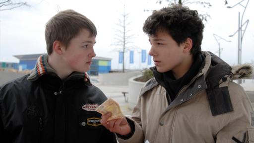 Ein Jugendlicher  (Lukas Kieback, rechts) hält einem anderen (Maximilian Werner) einen Geldschein hin. Sie sehen sich an.