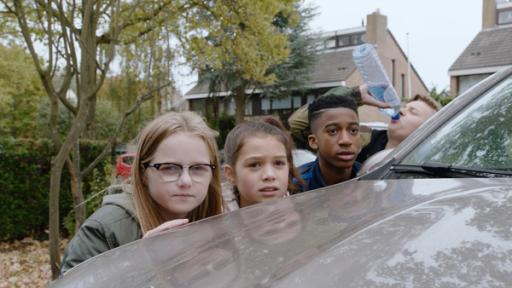 Vier Kinder verstecken sich hinter einem Auto.