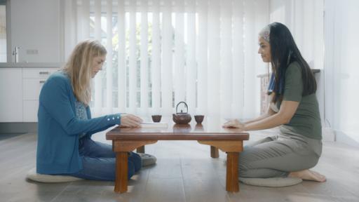 Margreets Mutter und Irma hocken an einem Tisch auf dem Fußboden