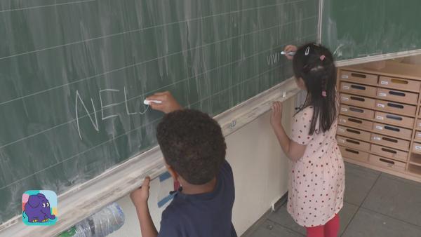 Kinder zeigen dir ihre Schule und den Klassenraum, in dem sie Unterricht haben. Sie schreiben mit Kreide an die Tafel. | Rechte: KiKA