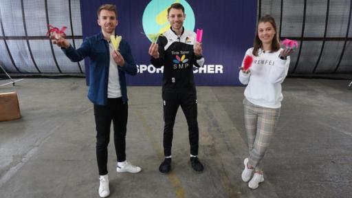 Stefan (links), David Zentarra (Mitte) und Laura (rechts) stehen vor dem Sportmacher-Logo und halten Federbälle in den Händen.