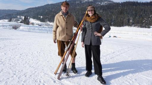 Die Sportmacher: Skilehrer Tissi und Moderatorin Laura stehen in historischer Skikleidung aus den 1950er mit Skier in der Hand im Schnee.