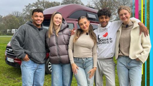 Emma, Sofia, Toni, Malik und Chinedu stehen vor ihrem Camper auf einer Wiese