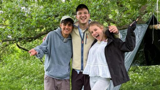 Dominik, Philipp und Pauline stehen vor einem selbst gebauten Shelter