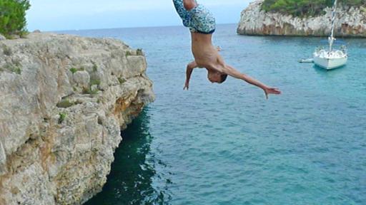 Ein Junge springt von einer Klippe ins Meer.