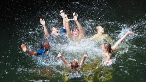 Die sechs Jugendlichen schwimmen in einem Felspool und strecken lachend die Hände hoch.