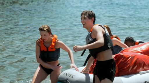 Die sechs Jugendlichen ziehen das Gummiboot mit den Rucksäcken darin aus dem Meer an Land. Im Bild vorne sind Tania und Ben in schwarz-orangen Schwimmwesten.