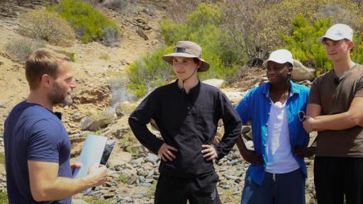 Wildniscoach Tobi steht vor Ben, Isaak und Bruno, hält eine Landkarte in der Hand und erklärt die Navigation.