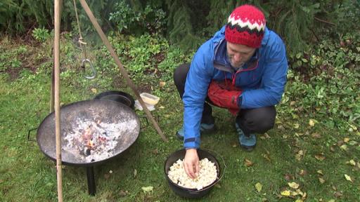 Coach Tobias nimmt frisches Popcorn aus einem Topf, der neben der Feuerschale steht.