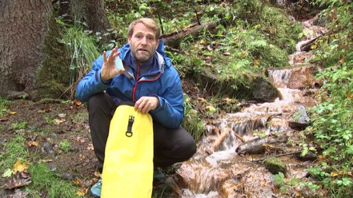 Wildniscoach Tobias kniet mit wasserdichtem Sack und Outdoor-Seife neben einem Bachlauf