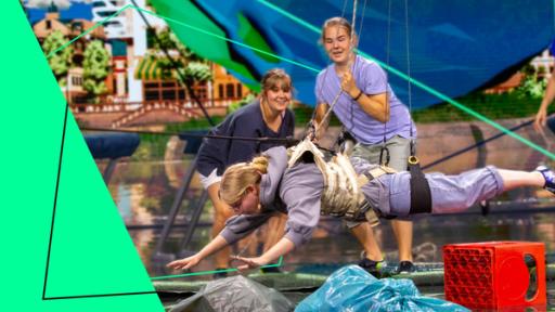 Die „Guardians of Earth” v. l. n. r. Lukas, Annika und Jakob halten Lucy an einem Klettergurt waagerecht über Wasser. In diesem Fluss, der an eine Stadt mit Uferpromenade grenzt, befindet sich Müll und Plastikgegenstände, die rausgefischt werden sollen. Mit dabei Moderatorin Jessica Schöne. Im Hintergrund sieht man die untere Hälfte einer Erdkugel.