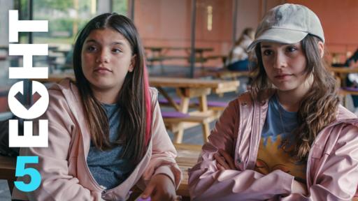 Zerda und Leyla sitzen in der Schule nebeneinander. Sie tragen das gleiche Outfit.